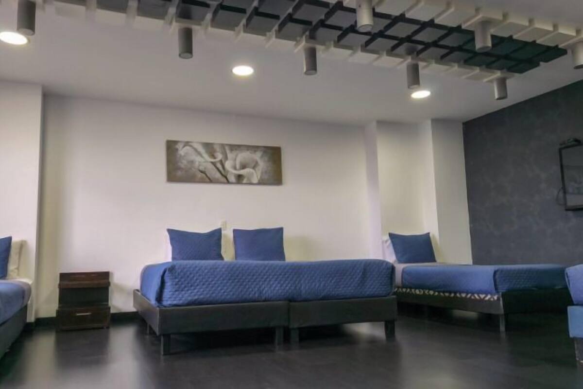 A hotel room with three beds, a ceiling with recessed lighting, and a wall-mounted artwork.