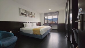 A hotel room with a bed, a desk, a chair, a window with a city view, and a refrigerator. - Hotel City Center Corferias (Bogotá)