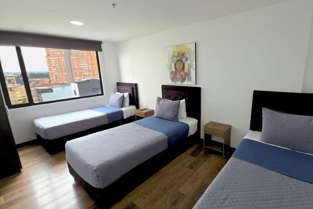 A hotel room with three beds, a large window offering a city view, and a painting on the wall.