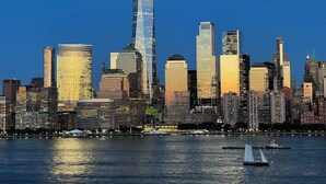 A city skyline with a prominent skyscraper, various other high-rise buildings, and a body of water with boats. - Lovely Loft Near NYC, EWR &
American Dream Mall (Newark)