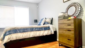 A bedroom with a bed, a dresser, a mirror, and a window with blinds. - Lovely Loft Near NYC, EWR &
American Dream Mall (Newark)