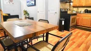 A dining area with a wooden table and chairs, a kitchen with wooden cabinets and appliances, and a television on the wall. - Lovely Loft Near NYC, EWR &
American Dream Mall (Newark)