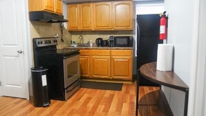 A compact kitchen with wooden cabinets, a stove, a microwave, and a sink. - Lovely Loft Near NYC, EWR &
American Dream Mall (Newark)