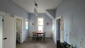 Uma área de refeições com mesa e cadeiras, uma janela com luz natural e duas obras de arte emolduradas na parede.