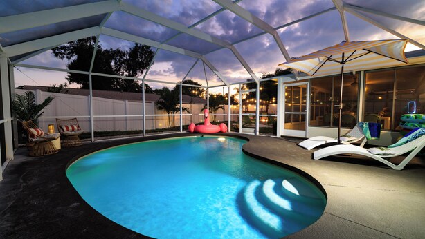 A covered outdoor swimming pool with lounge chairs and a glass enclosure. - Costal Escape: Heated Pool~Tiki Bar~Hot Tub~Fire Pit~Acarde~Pool Table (Bradenton)