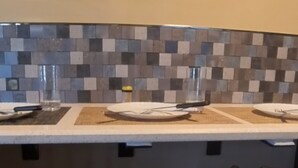A kitchen with a tiled backsplash, a white countertop, and three bar stools. - 4Bd 2Ba 7 Person Sleeper-  King Bed (Somerdale)