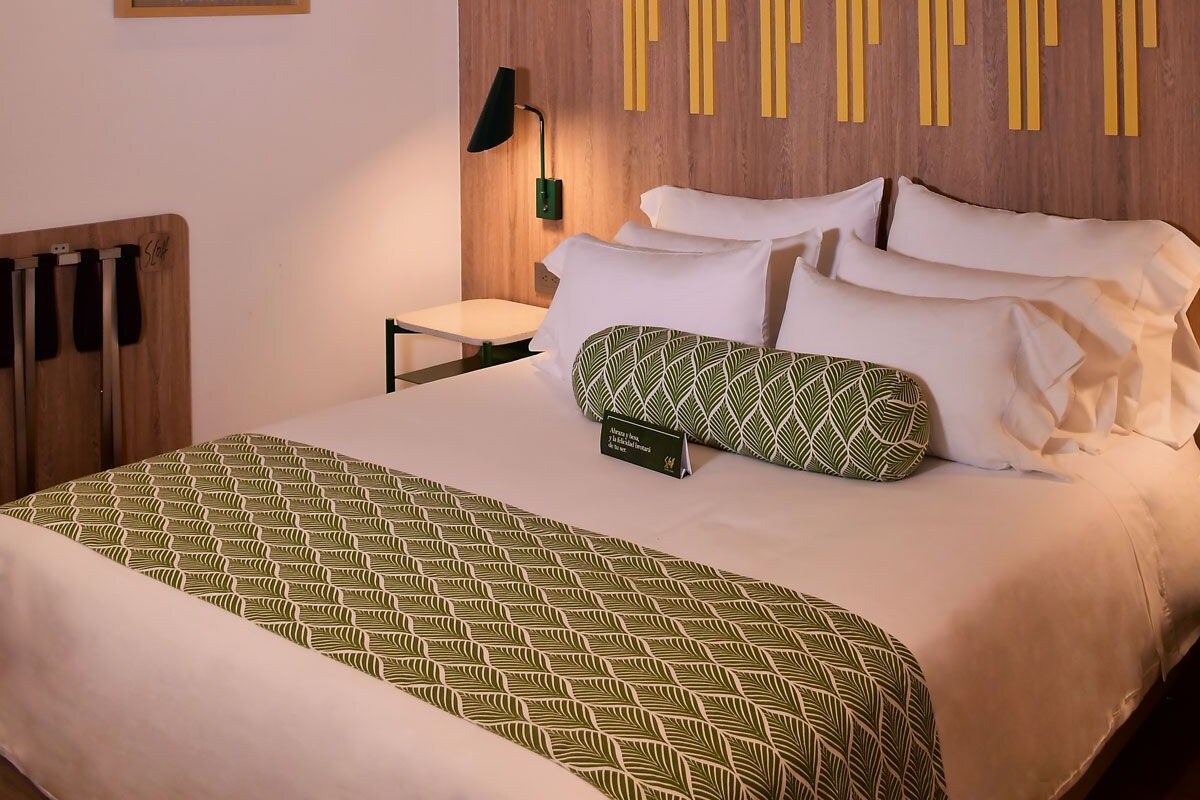Une chambre d’hôtel moderne équipée d’un lit, d’une table de chevet, d’une lampe et d’une œuvre d’art accrochée au mur.