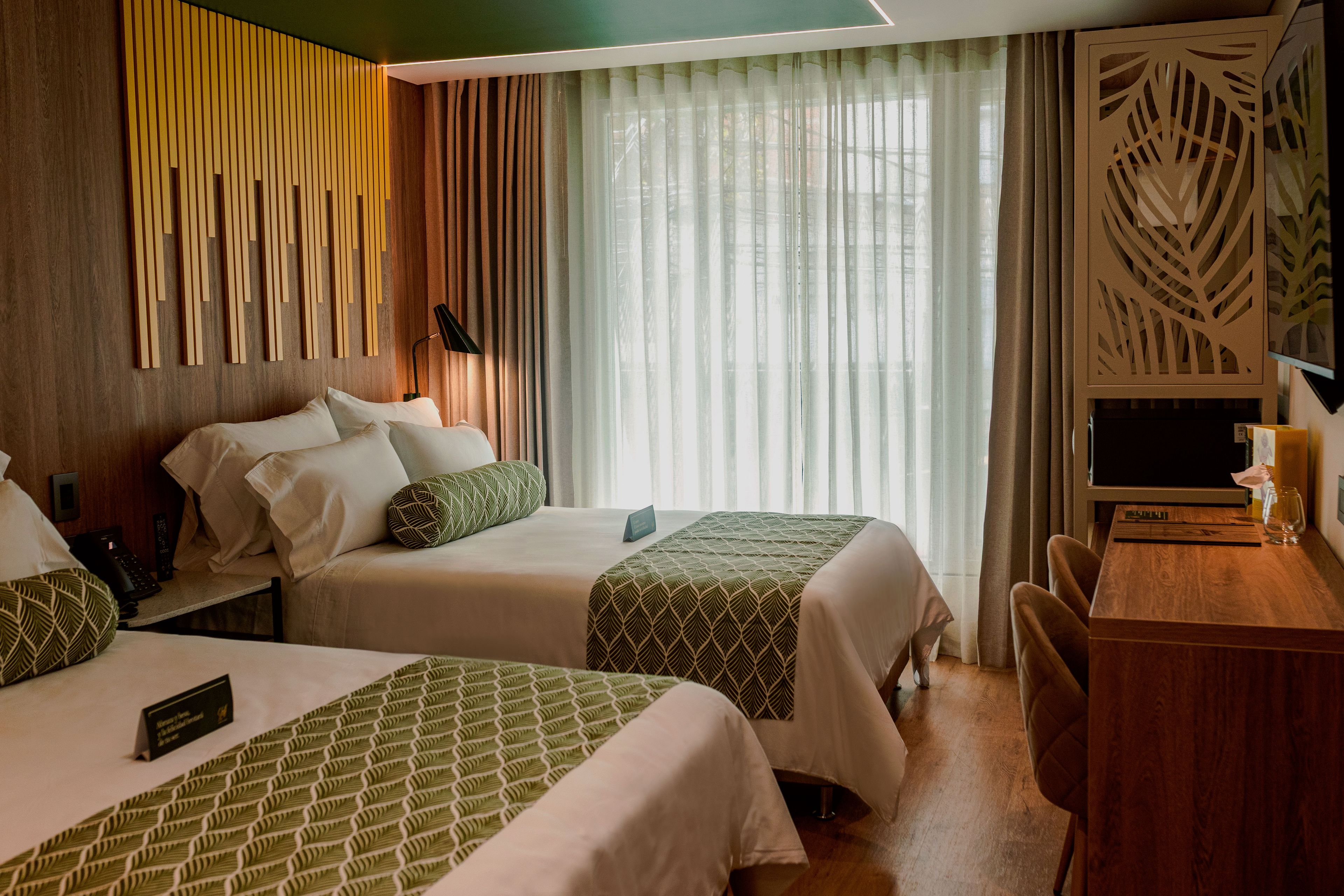 Una habitación de hotel con dos camas, un escritorio y un ventanal con cortinas.