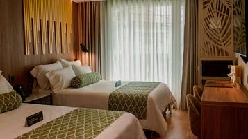 Una habitación de hotel con dos camas, un escritorio y un ventanal con cortinas.