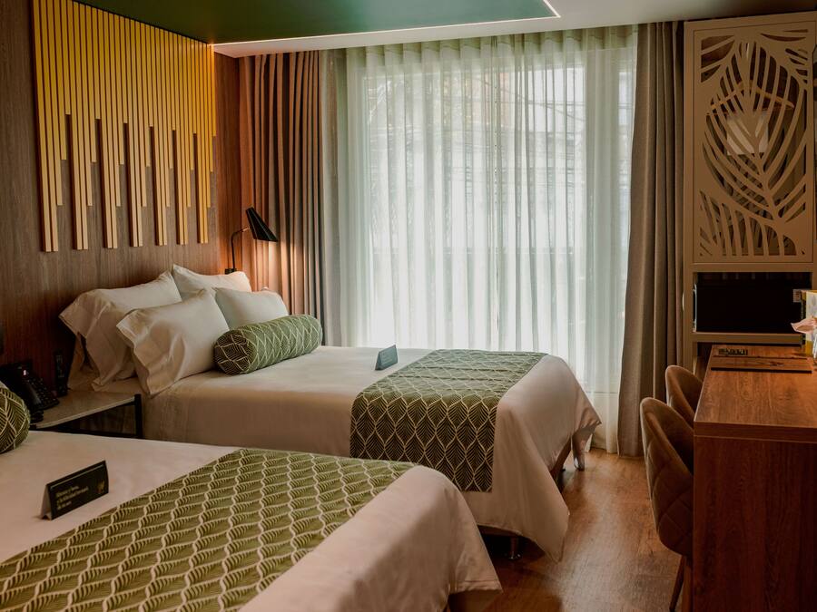 Una habitación de hotel con dos camas, un escritorio y un ventanal con cortinas.