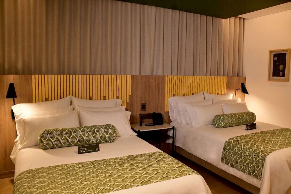 A hotel room with two beds, each with a headboard, bedside tables, and lamps.