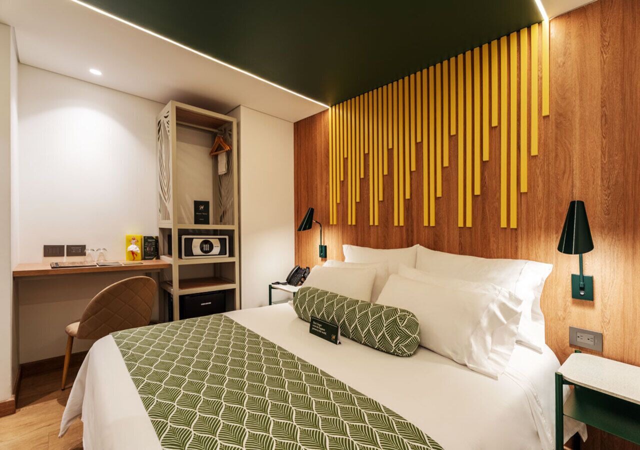 A hotel room with a bed, a desk, a chair, a wardrobe, and a wall with vertical wooden slats.