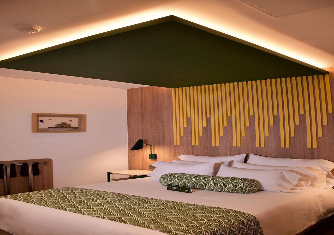 Et moderne hotelværelse med en seng, et natbord, en lampe og et billede i ramme på væggen.