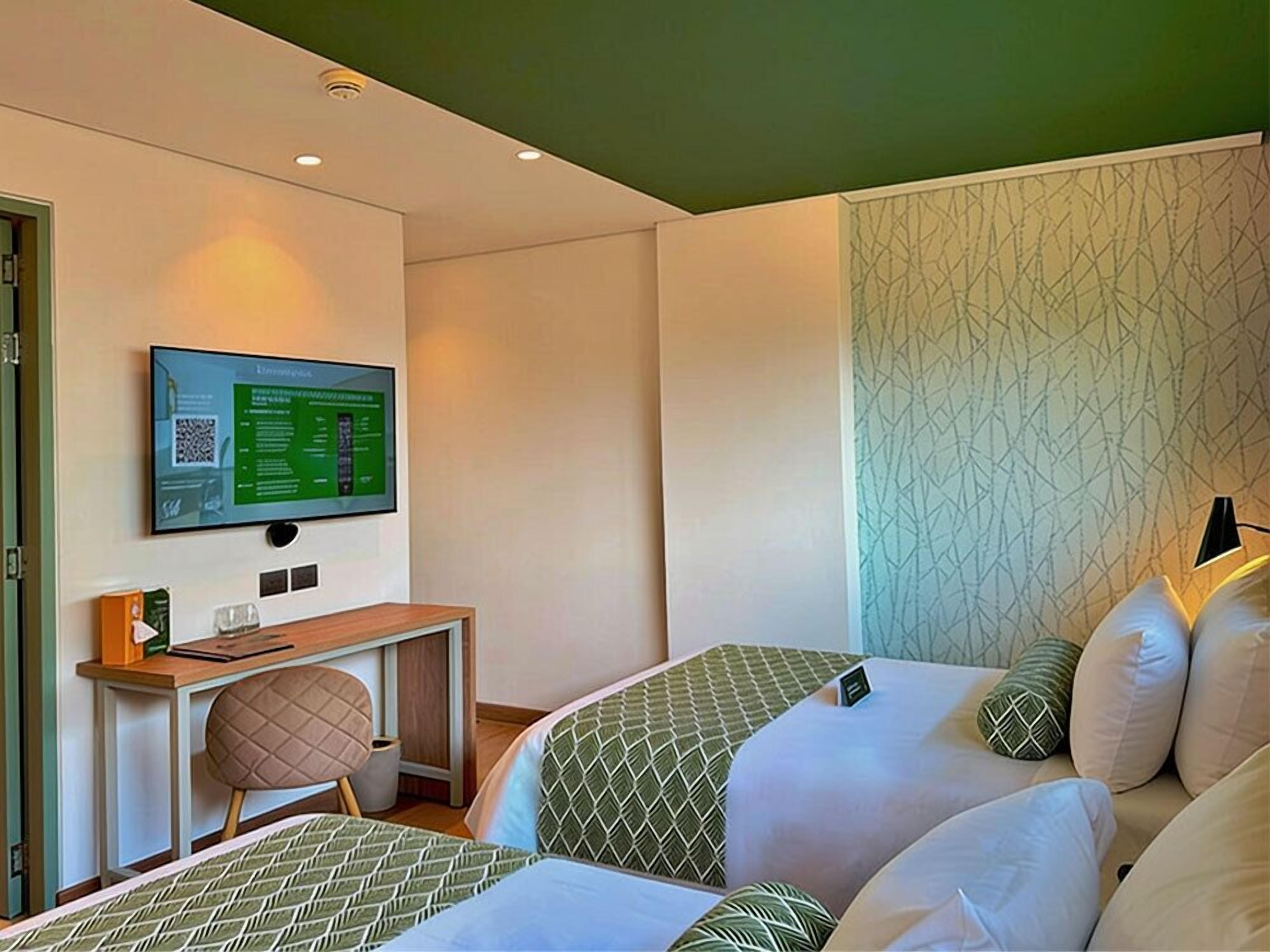 Una habitación de hotel con dos camas, un escritorio, un televisor y un papel tapiz estampado.