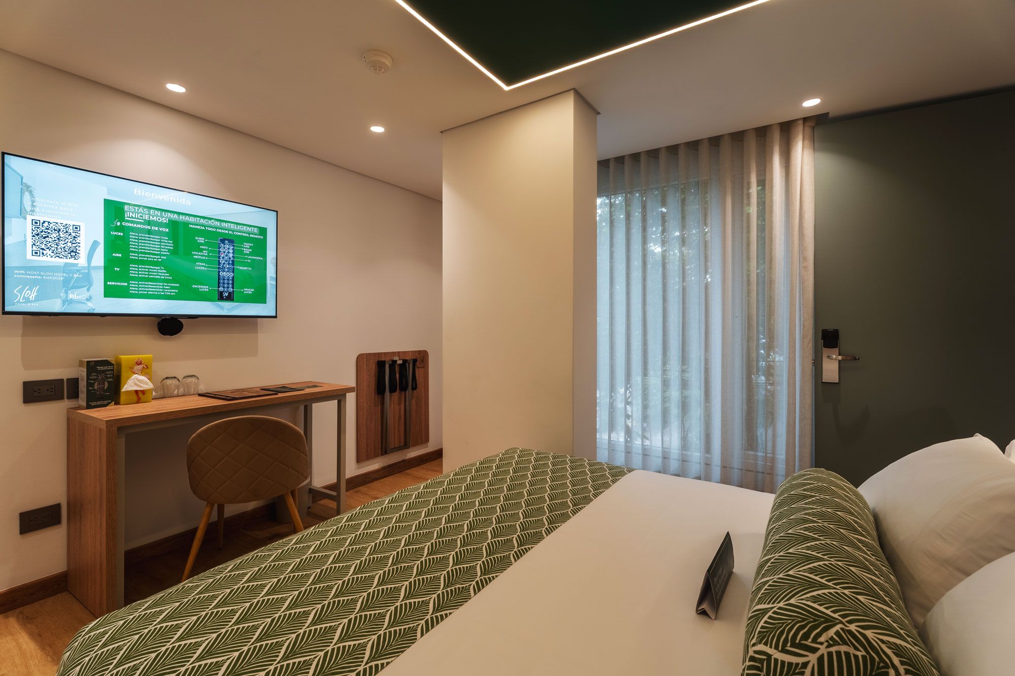 Ett modernt hotellrum med en säng, ett skrivbord, en stol, en tv-skärm som visar information om rummet och ett fönster med gardiner.