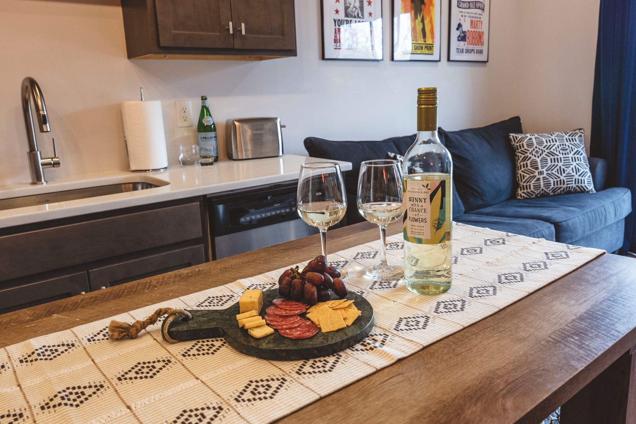 A kitchen counter with a cheese and fruit platter, two wine glasses, and a bottle of wine.