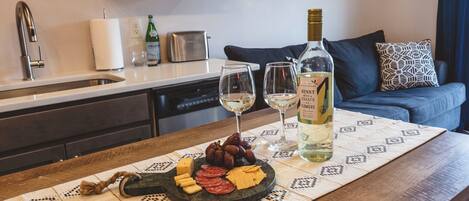 A kitchen counter with a cheese and fruit platter, two wine glasses, and a bottle of wine.