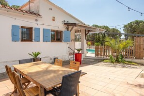 Une terrasse avec une table et des chaises en bois, un pot de fleurs rouge et une clôture en bois.