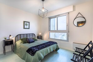 Ein Schlafzimmer mit Bett, Nachttischen, einem Fenster, einer Pendelleuchte und einem Spiegel an der Wand.