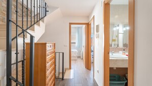 A staircase with a wooden finish and black metal railings, leading to a bedroom with a bed and a bathroom with a sink and a mirror. - Holiday Home 'Cozy Townhouse In Soneja' with Mountain View, Wi-Fi and Air Conditioning (Soneja)