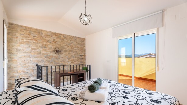 A bedroom with a bed, a stone wall, a balcony, and a hanging light fixture. - Holiday Home 'Cozy Townhouse In Soneja' with Mountain View, Wi-Fi and Air Conditioning (Soneja)
