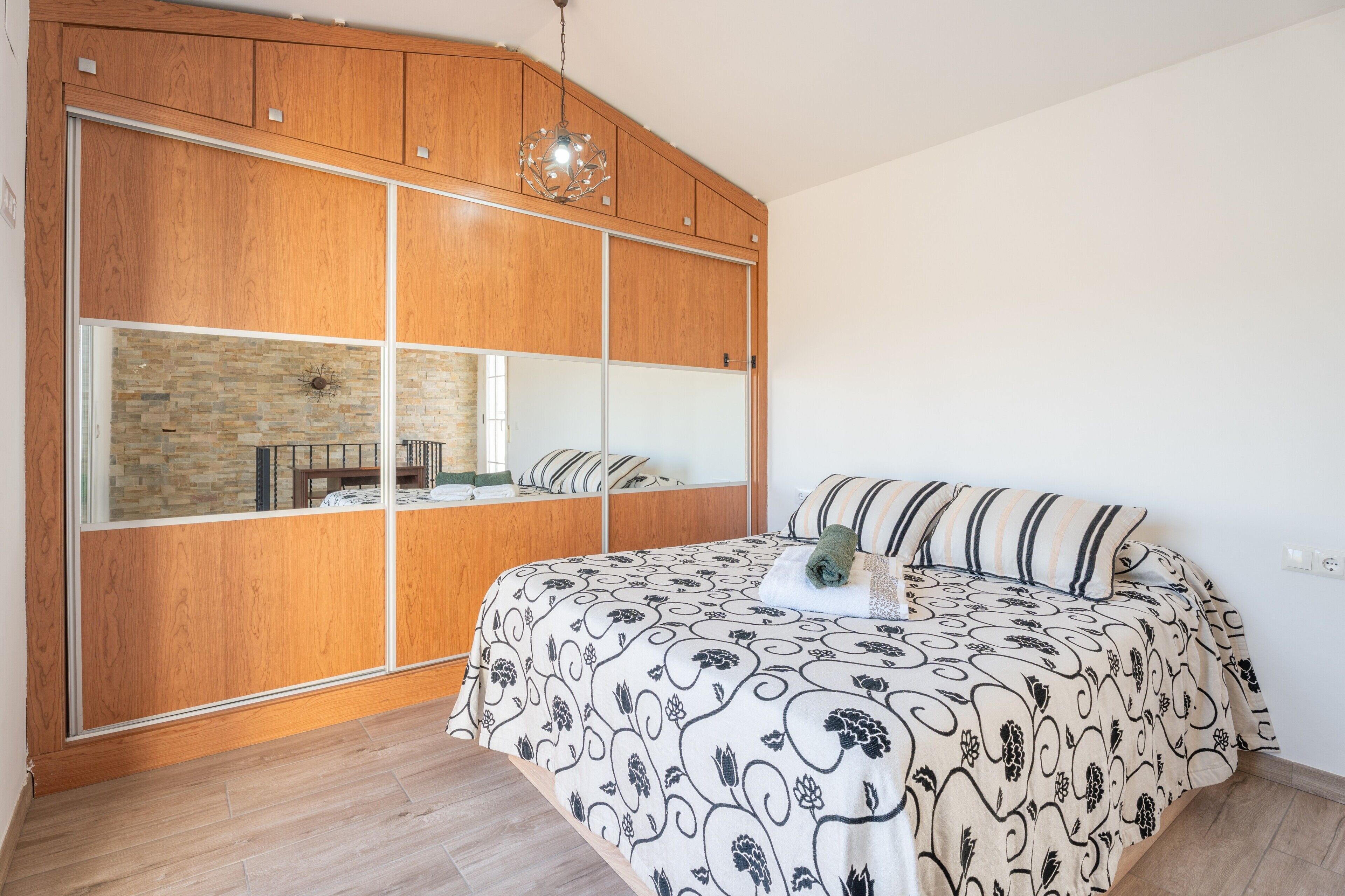 A bedroom with a large bed, wooden wardrobe, and a stone wall.