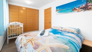 A bedroom with a bed, a crib, wooden wardrobes, and a beach-themed painting. - Holiday Home 'Cozy Townhouse In Soneja' with Mountain View, Wi-Fi and Air Conditioning (Soneja)