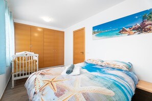 Une chambre à coucher avec un lit, un berceau, des armoires en bois et un tableau sur le thème de la plage.