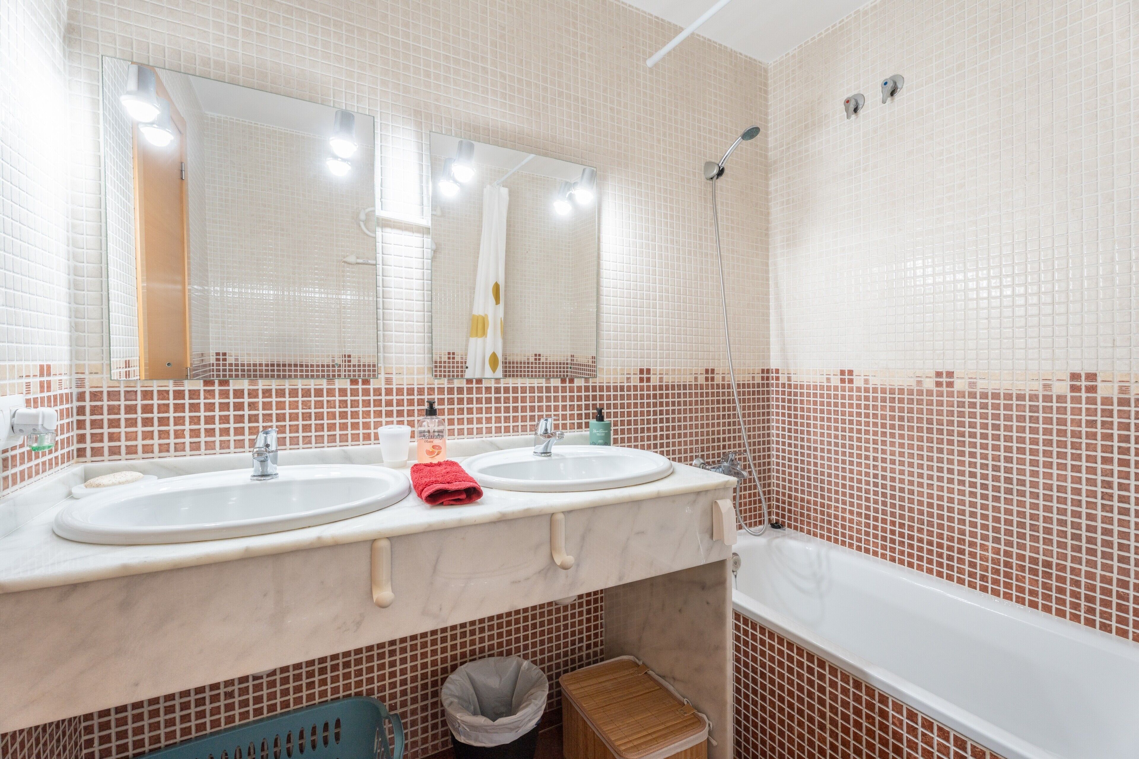 Un baño con dos lavamanos, un espejo, una ducha y un cubo de basura.