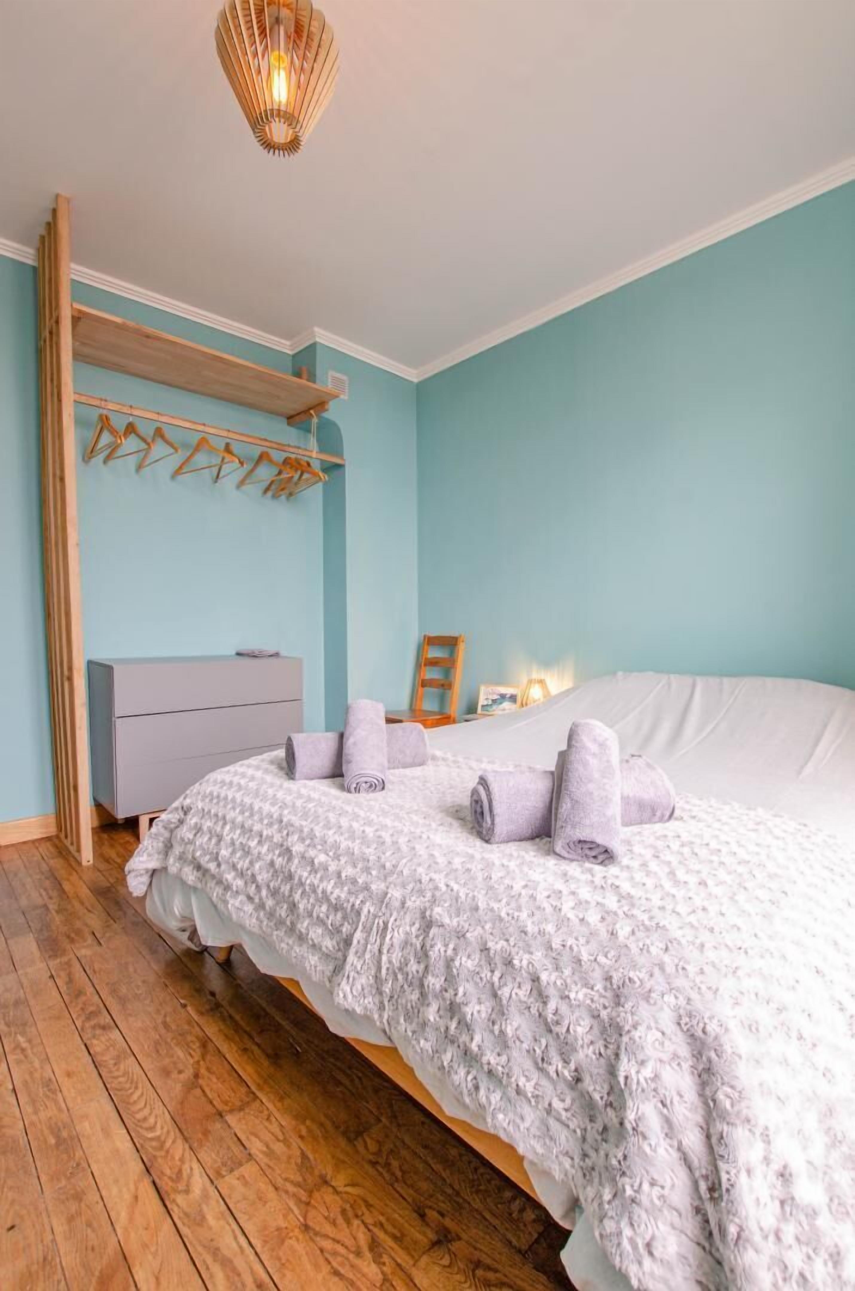 A bedroom with a large bed, a wooden shelf, a dresser, and a hanging light fixture.