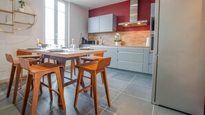 A modern kitchen with a dining table and chairs, a refrigerator, and a red accent wall. - L'Art Déco - TROYES - City break (TROYES)