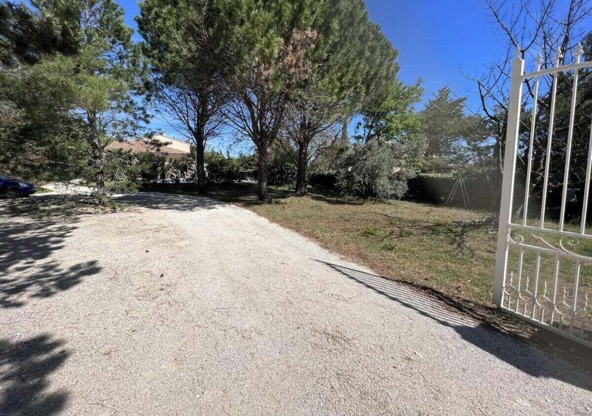 A gravel driveway leading to a gated area with trees and a clear sky.