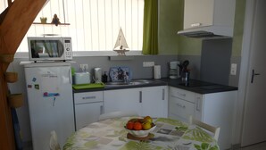 Een kleine keuken met een magnetron, broodrooster en spoelbak. Er staat een tafel met een fruitschaal en een stoel.