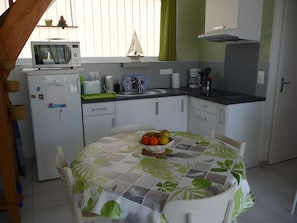 Cozinha compacta com micro-ondas, torradeira e pia. Há uma mesa com uma fruteira e uma cadeira.