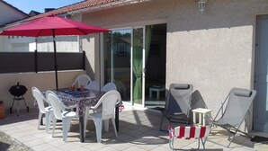 Een terras buiten met een tafel, stoelen, een barbecue en een schuifpui.