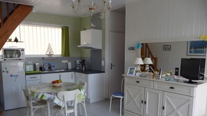 Een kleine keuken met een eethoek, een koelkast, een magnetron, een spoelbak en een eettafel met stoelen.