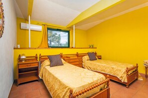 Une pièce avec deux lits en bois, une fenêtre avec des rideaux, une petite table et un climatiseur fixé au mur.
