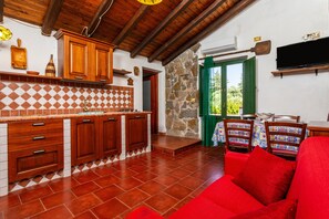 Eine Küche mit Holzausstattung und einer gefliesten Rückwand, ein Essbereich mit Tisch und Stühlen sowie ein rotes Sofa.