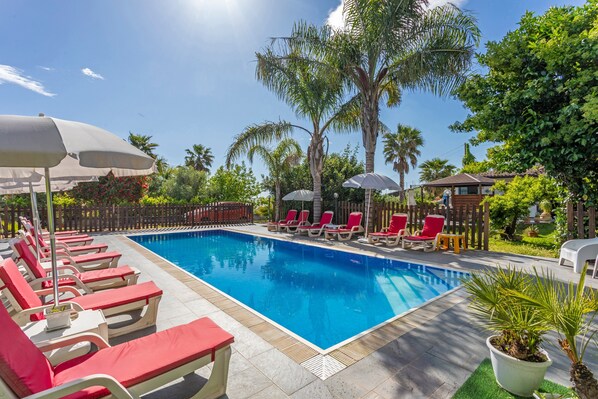 A swimming pool with lounge chairs and umbrellas, surrounded by palm trees and greenery.