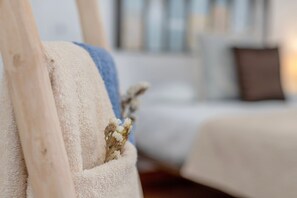 A close-up of a white, textured fabric with a dried flower, part of a room with a blurred background.