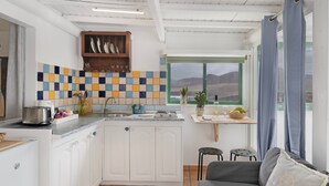 A compact kitchen with white cabinets, a tiled backsplash, a window with a view, and a grey sofa with a cushion. - Vacation 'Dangminzheng Atic' with Mountain View and Wi-Fi (Caleta de Caballo)