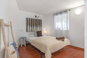 A bedroom with a bed, a nightstand, a lamp, a painting, and a window with curtains.