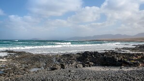 A rocky shoreline with waves, a clear sky, and distant mountains. - Vacation 'Dangminzheng Atic' with Mountain View and Wi-Fi (Caleta de Caballo)