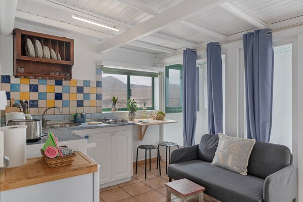 A kitchen with a window, a dining area with a table and chairs, and a grey sofa with a cushion.