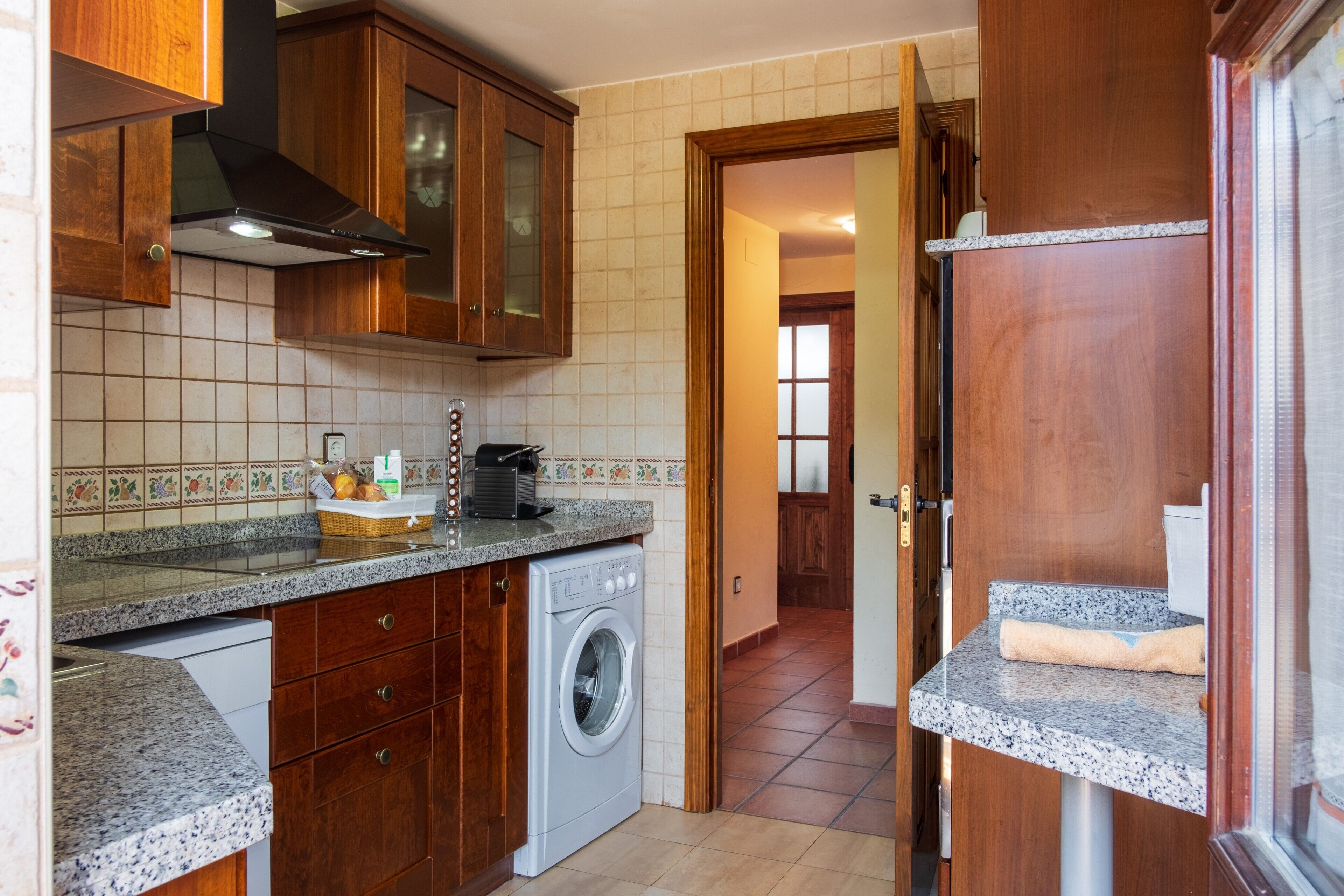 Cozinha com armários de madeira, máquina de lavar e bancada com cesta de frutas.