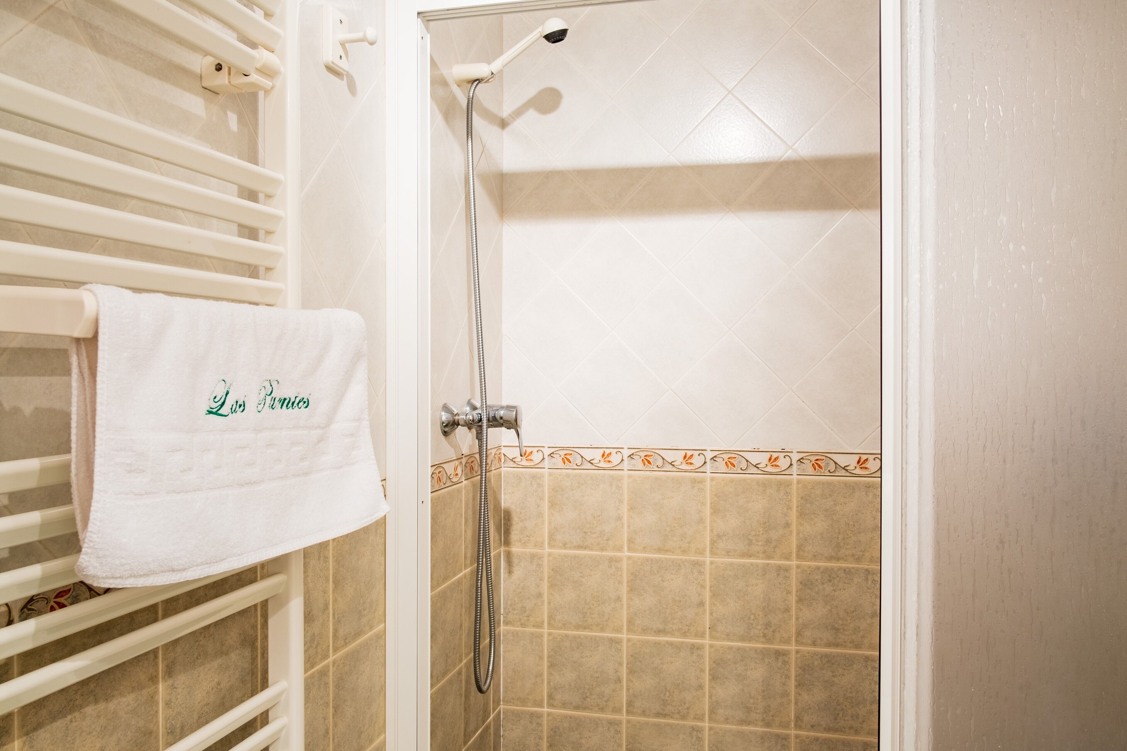 Een badkamer met een douche, een handdoekrek met een handdoek en betegelde muren.