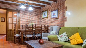 Un salon chaleureux avec un mur en briques, des meubles en bois, un canapé vert et un sol carrelé.