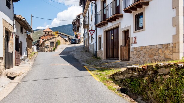 Une rue étroite bordée d’immeubles en pierre, un panneau de signalisation bien visible et une montagne en arrière-plan.