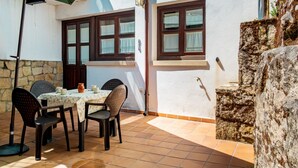 Une terrasse avec une table et des chaises, un parasol vert et un mur en pierre.