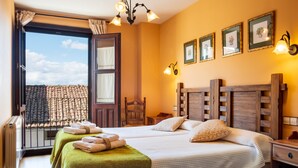 Une chambre d’hôtel avec deux lits, un balcon, une tête de lit en bois et des tableaux encadrés au mur.
